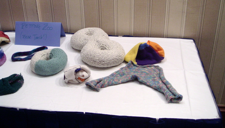 closeup of the right half of the petting zoo: right to left, a seven-colored fleece torus, a hyperbolic pair of pants, a two-holed torus, K_6 embedded on a projective plane, a torus, a mobius band, and a projective plane.